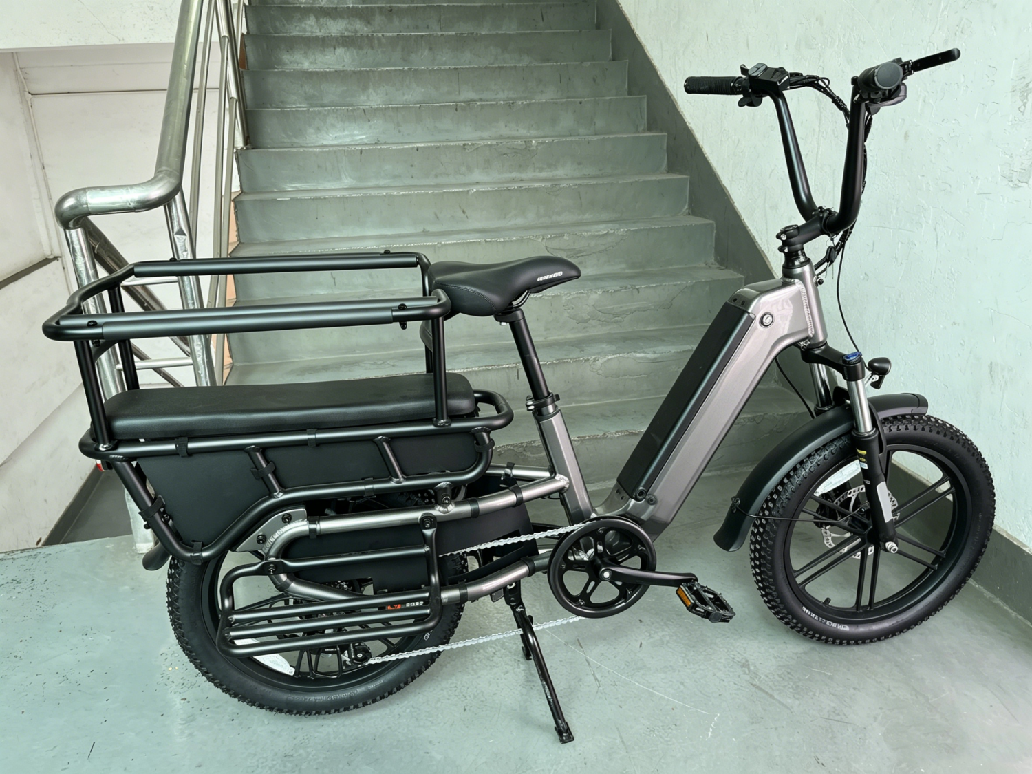 Vélo électrique gris avec coussin de siège arrière, barres de sécurité, repose-pieds