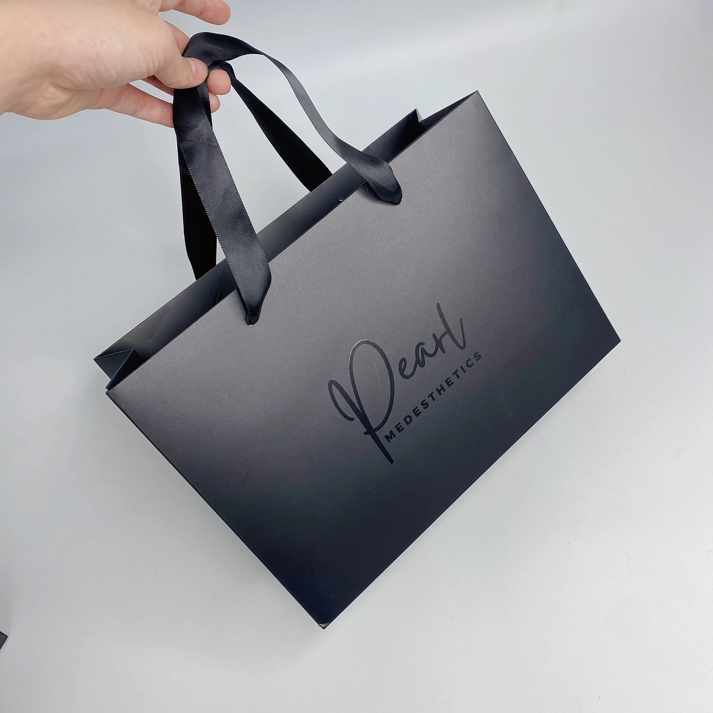 Bolsa de papel de lujo con impresión personalizada para compras, bolsas de papel con asa y lazo, color negro, con tu logotipo, venta al por mayor