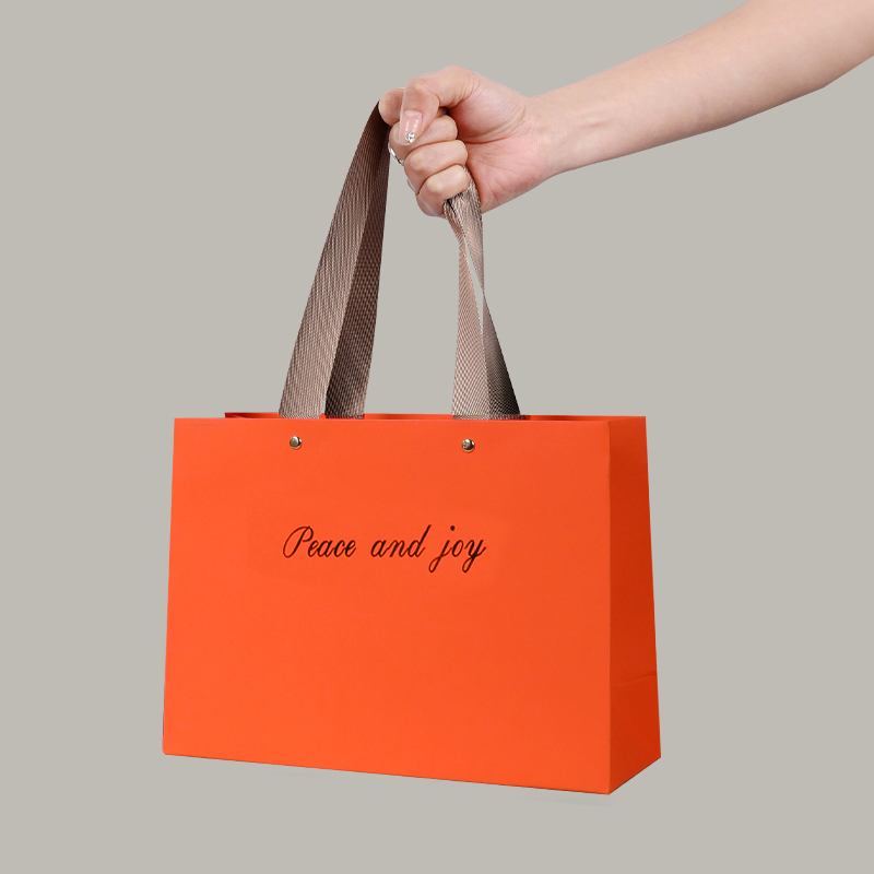 Bolsa de papel de pulpa de madera virgen naranja con letras doradas en relieve.