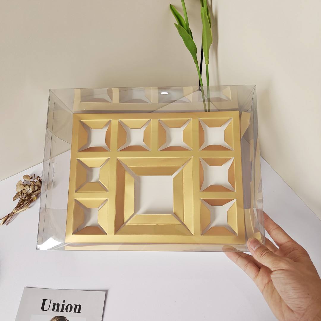 Boîte à gâteaux transparente en papier, compartimentée en 8 petits gâteaux carrés dorés.
