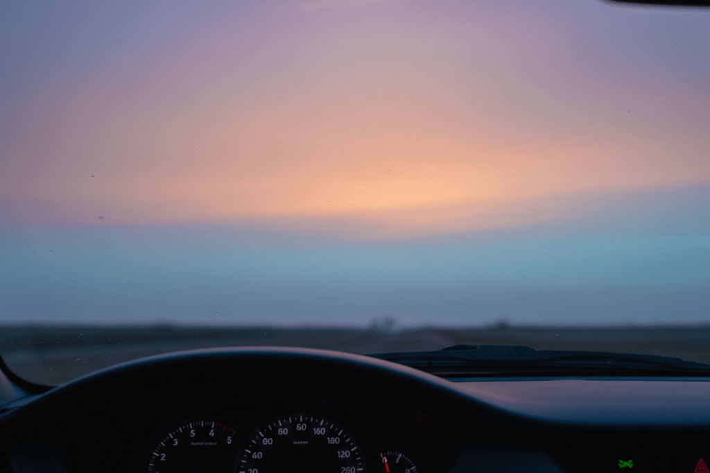 Medium shot of car dashboard at dawn showing sky with soft orange violet afterglow reflecting recent celestial fireball event