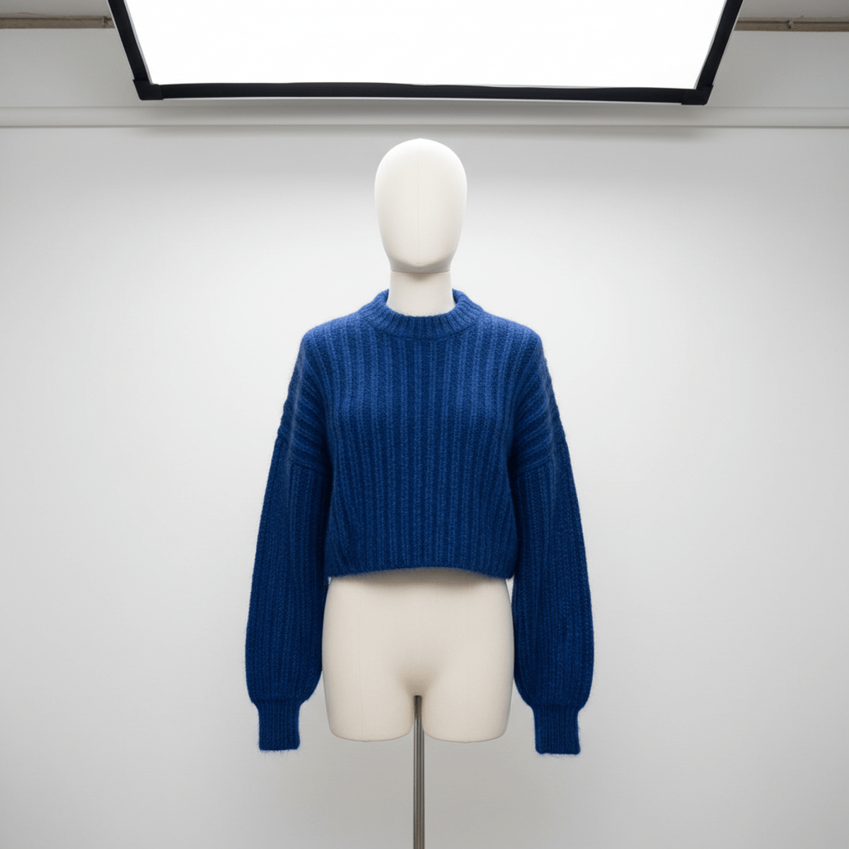 Bold cobalt blue cropped puffy ribbed cardigan draped on a mannequin, showing exaggerated texture.