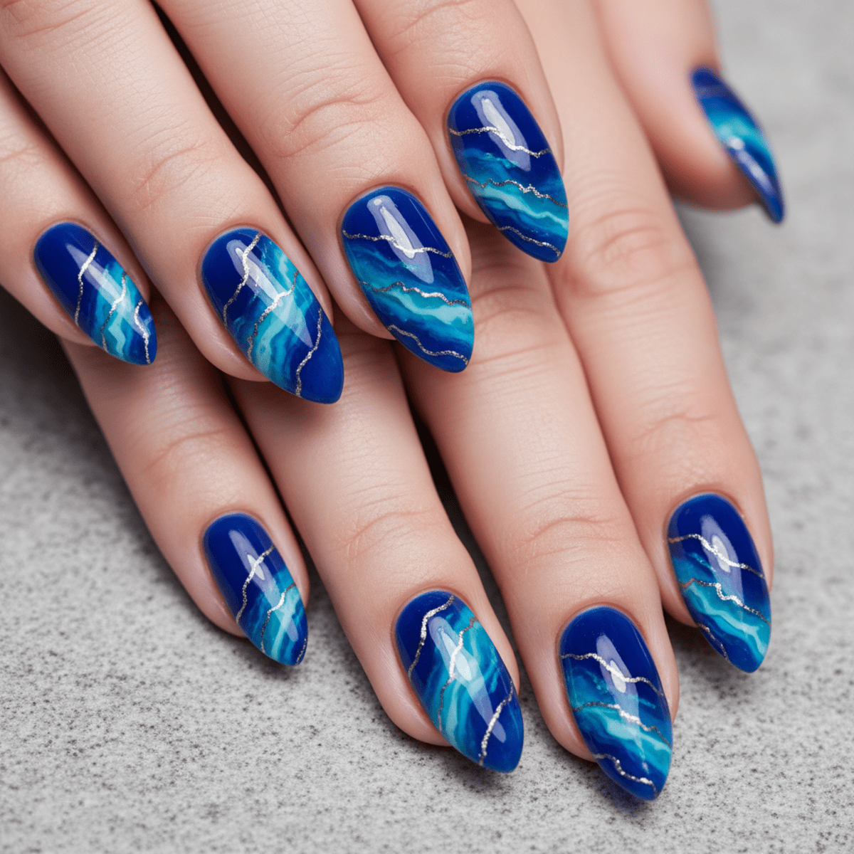 Geode-inspired manicure with deep blue gemstone patterns and silver crystal accents.