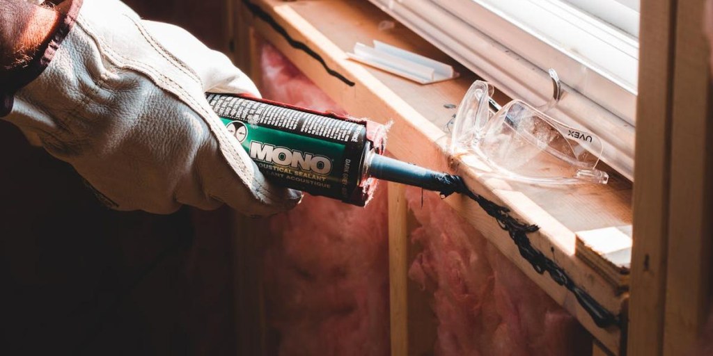 A contractor applying acoustic sealant caulk around a window frame