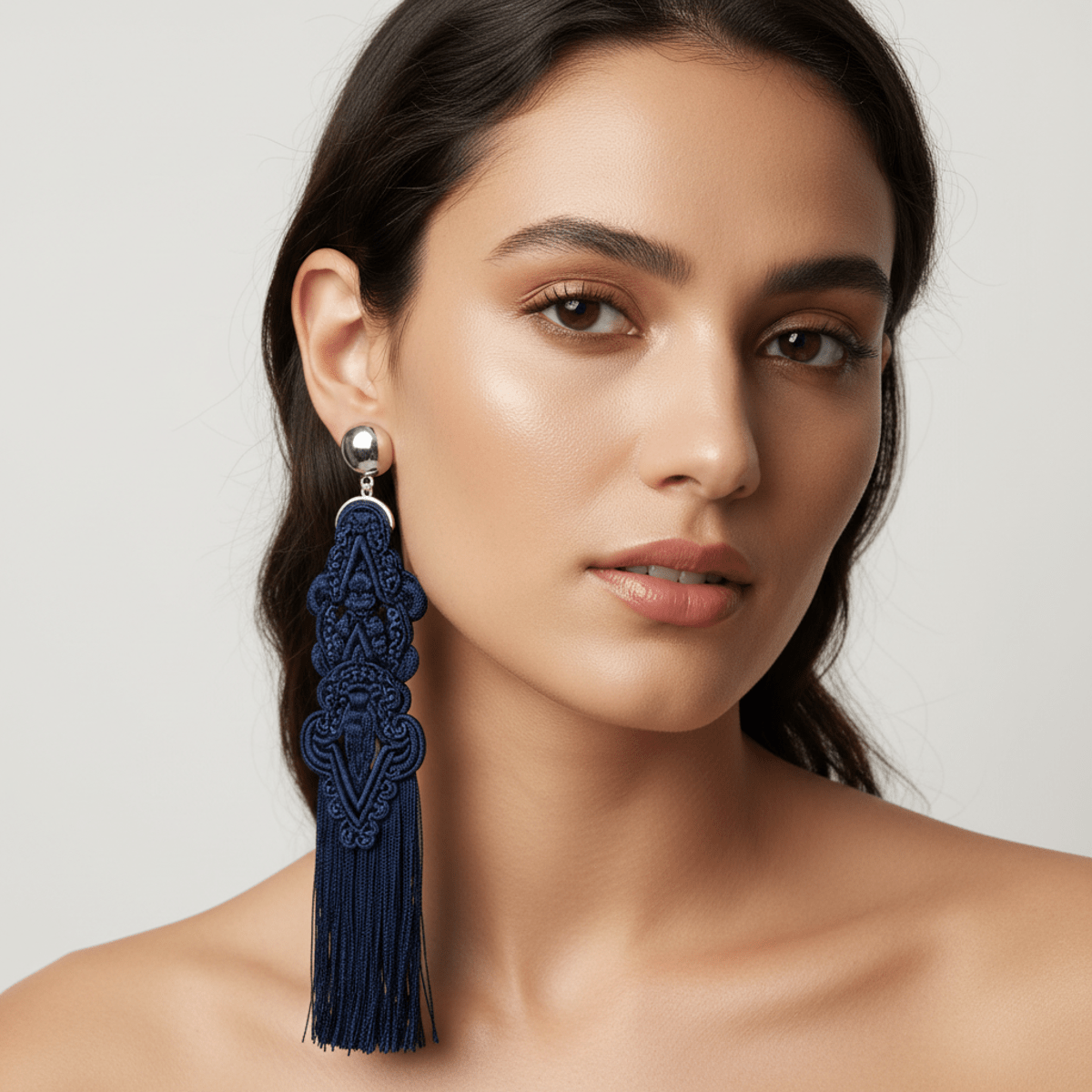 Close-up of a model wearing mismatched tassel earrings with silver hardware.