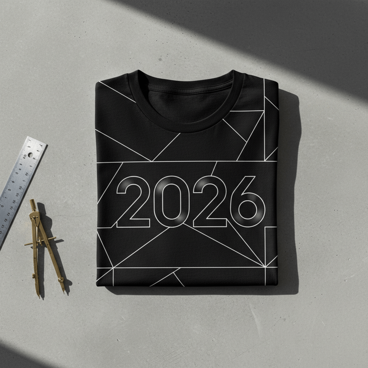 Black t-shirt with white geometric pattern on concrete with drafting tools.