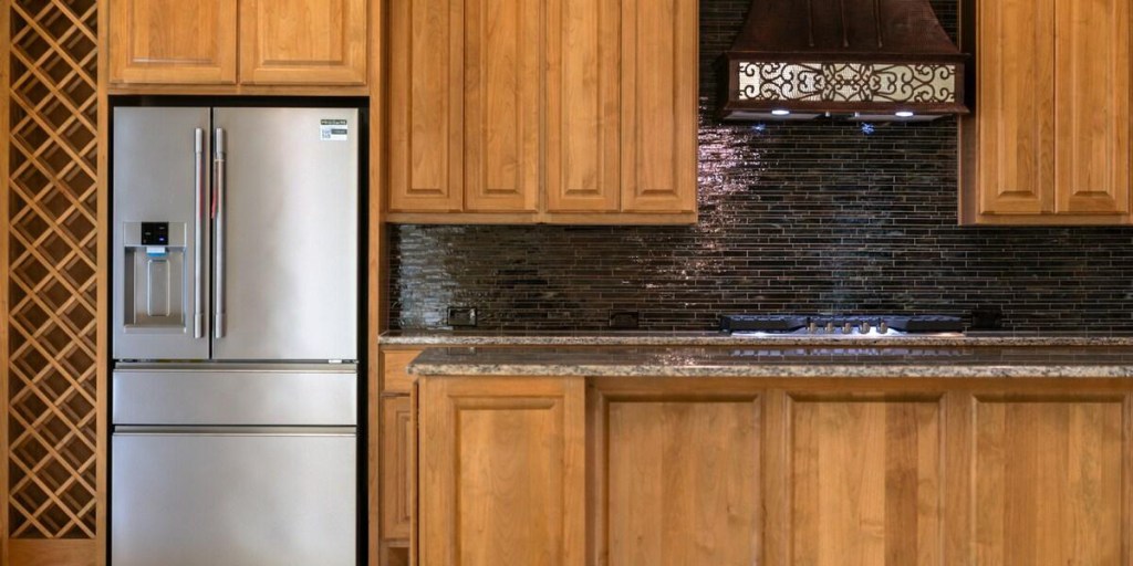 Wood kitchen cabinets with stainless refrigerator and black tile backsplash