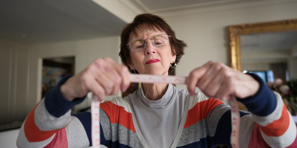 An elderly woman holding a tape to measure