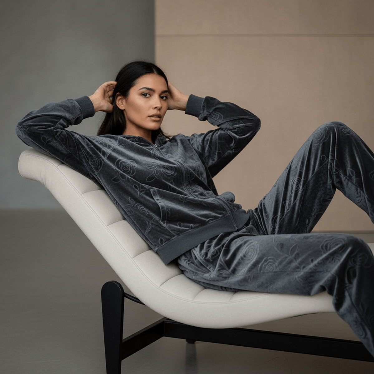 Luxury charcoal velvet tracksuit with embossed floral patterns, model lounging elegantly.