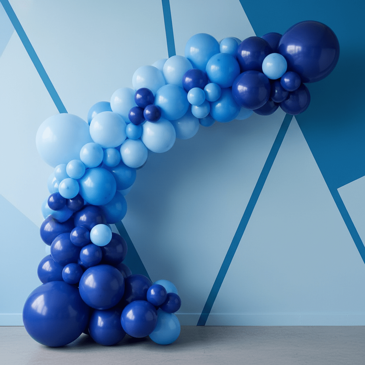 Flowing arc of matte, satin, and glossy blue balloons against a modern interior wall.
