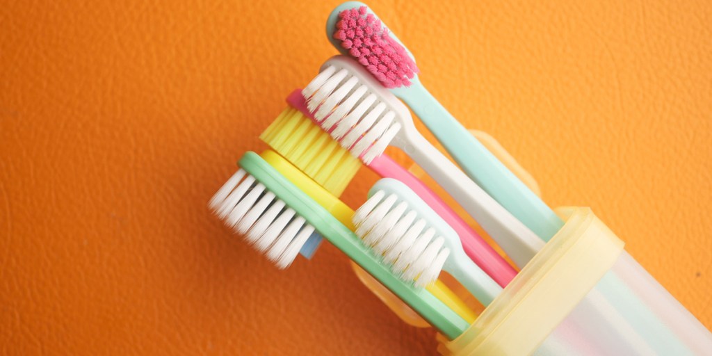 Vibrant toothbrushes in a clear holder on an orange backdrop
