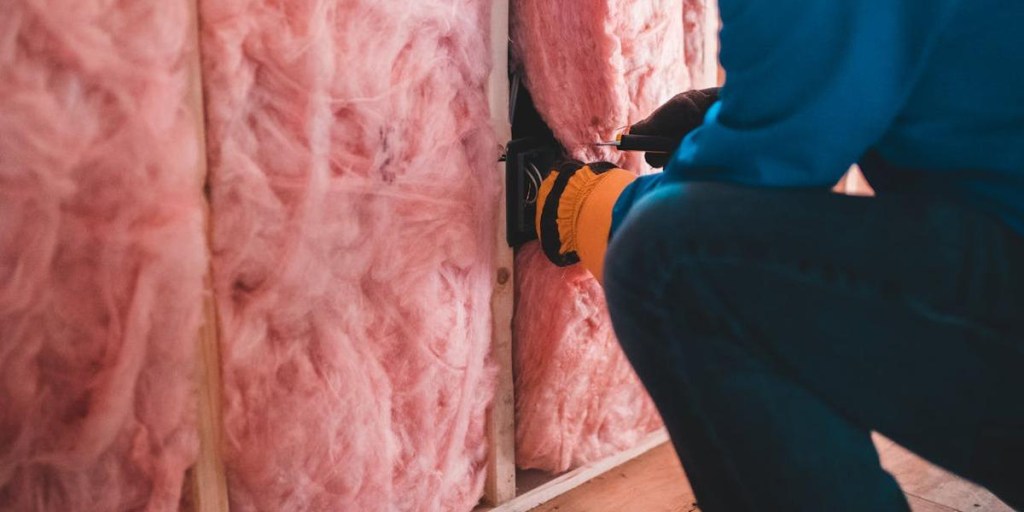 A contractor installing pink fiberglass insulation batts in wall studs