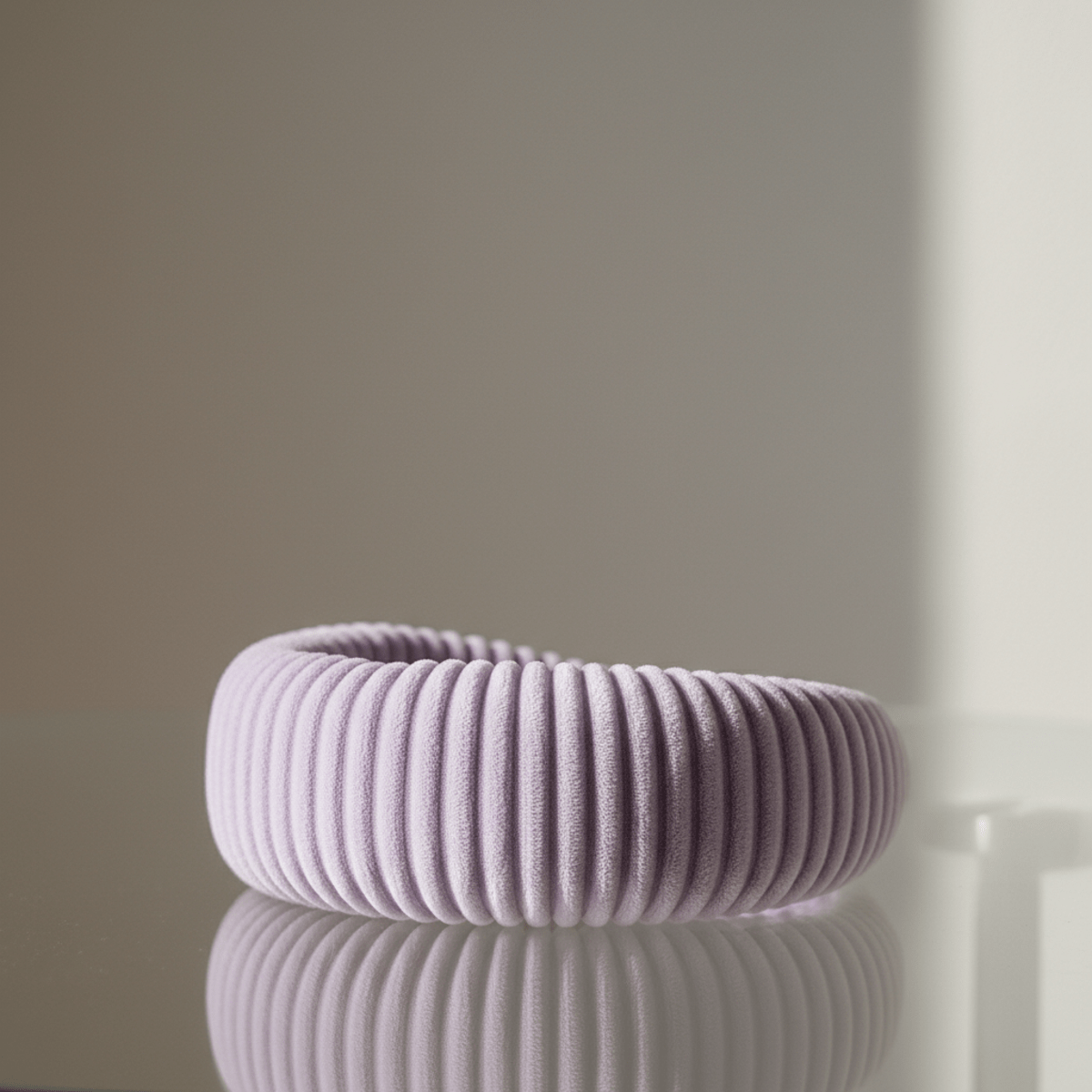 A soft, puffy ribbed headband in digital lavender rests on a polished glass surface.