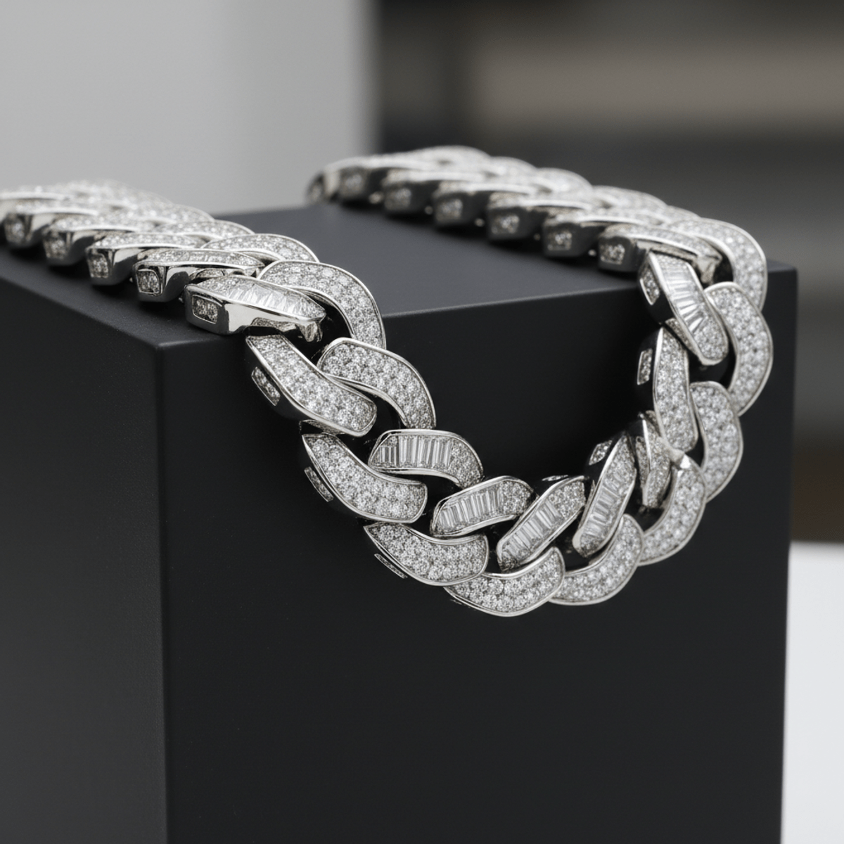 Bold Cuban link chain with baguette and round moissanite stones on black pedestal.