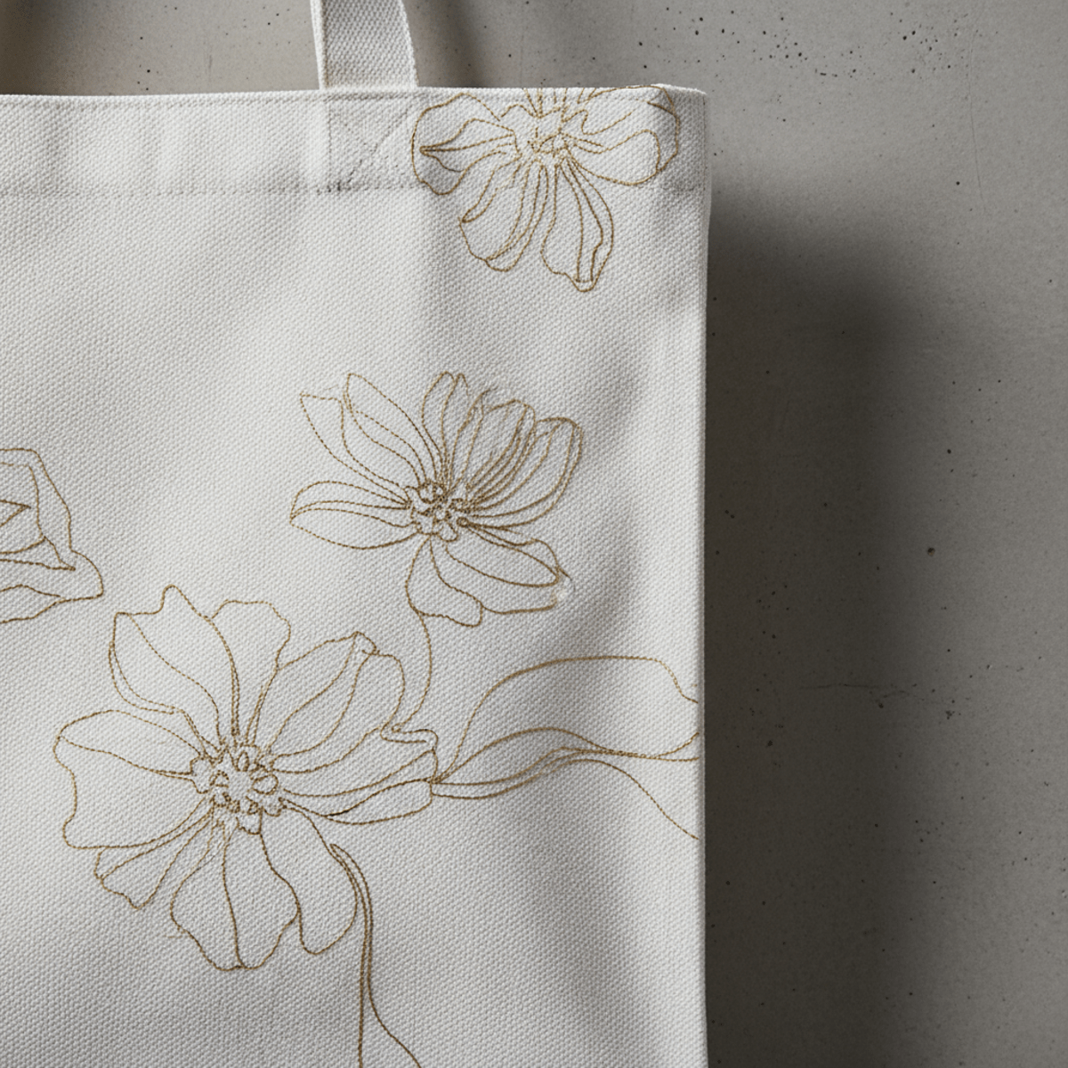 White canvas bag with gold floral embroidery hanging on a concrete wall.