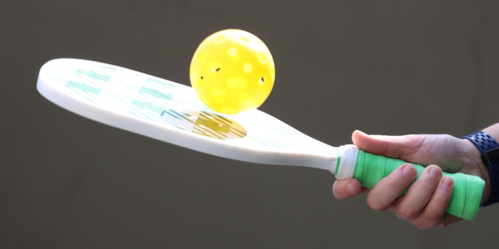 Person bouncing pickleball on paddle