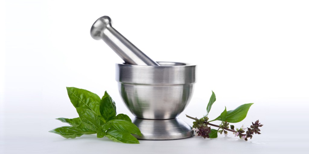 Stainless steel mortar and pestle with fresh herbs beside