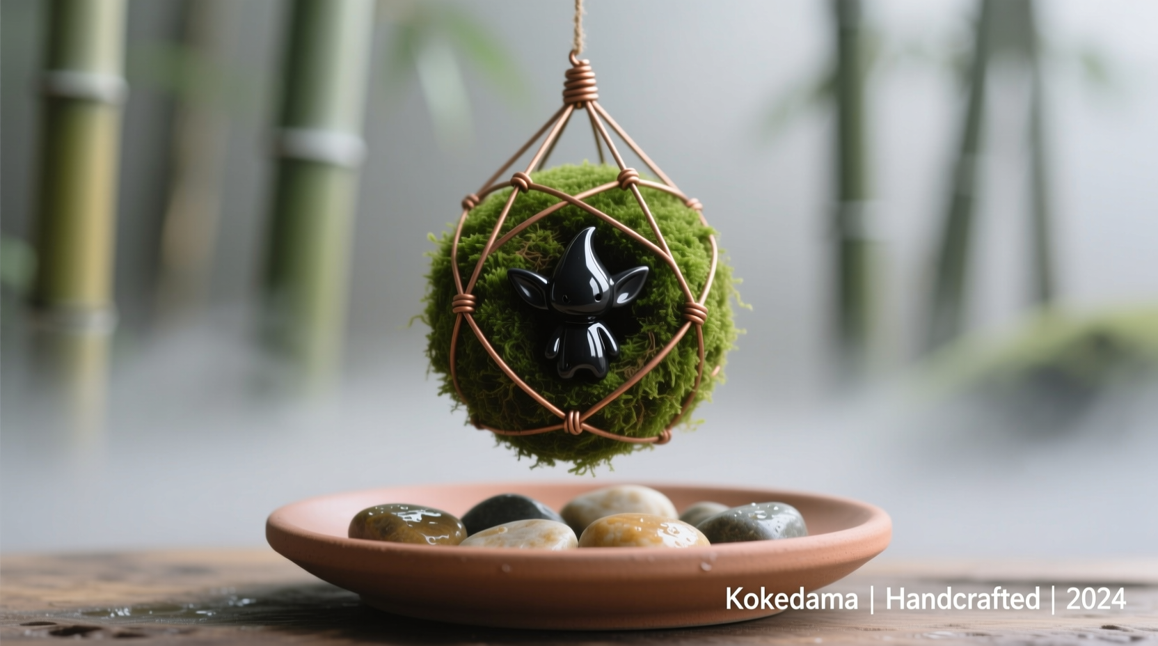 A hand-styled kokedama featuring a small, glossy black soot sprite polymer clay charm nestled in emerald moss, suspended by thin copper wire above a matte terracotta tray filled with damp pebbles