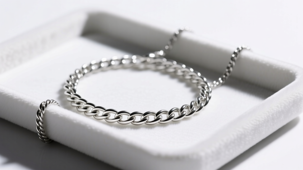 Close-up of a tangled 0.9mm sterling silver rope chain on a white velvet tray, illuminated by a focused overhead studio light