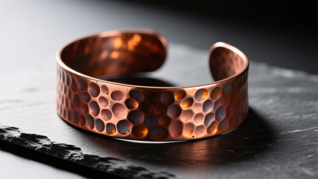 Hammered copper cuff bracelet on dark slate, warm directional light highlighting its natural reddish-brown oxidized patina finish.