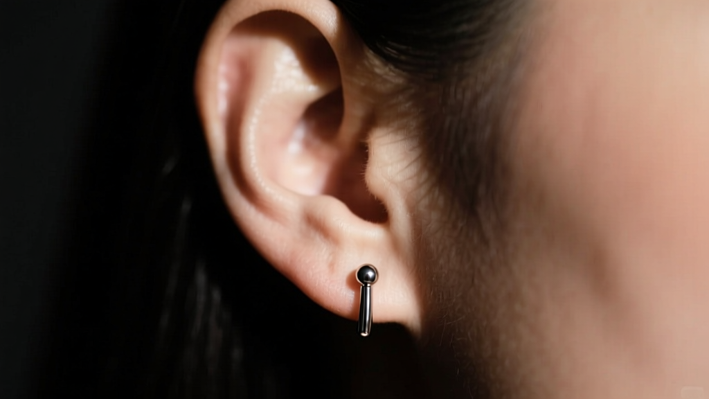 Left earlobe wearing a simple 18-gauge titanium stud earring, shown in moody cinematic lighting against a dark backdrop