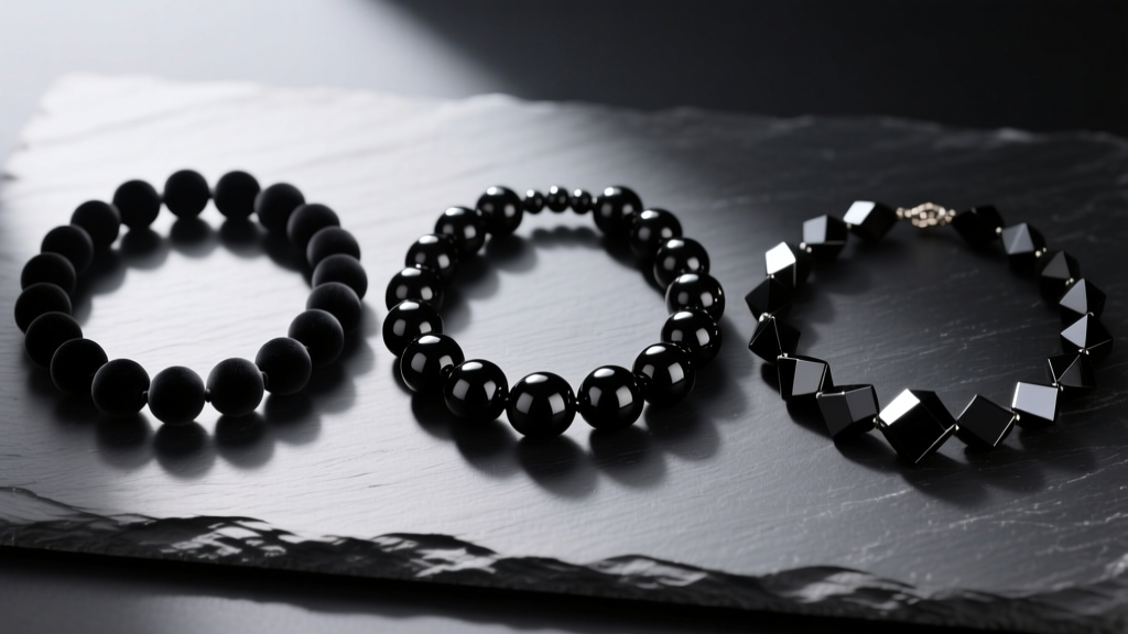 Flat lay of three black beaded mens necklaces: matte ebony, glossy obsidian, and faceted onyx resting on a dark slate surface