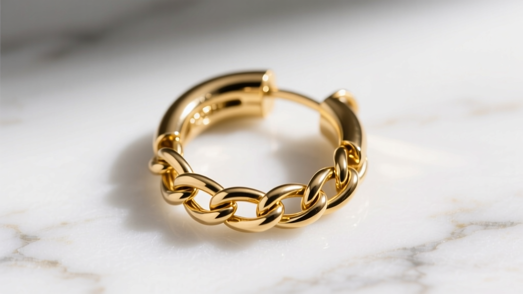 Macro shot of a 16-gauge solid gold huggie hoop with a clicker clasp and delicate cable chain detail on a white marble surface