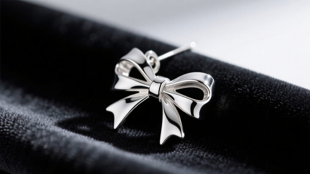 Macro shot of an Argentium silver bow drop earring on a dark cloth, highlighting intricate ribbon folds and bright metallic shine.