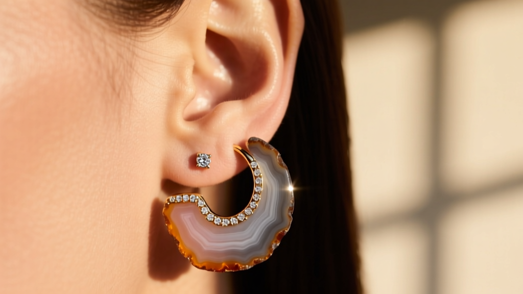 Close up of an ear wearing an 18-gauge raw agate slice huggie hoop earring with small diamond accents in warm natural sunlight