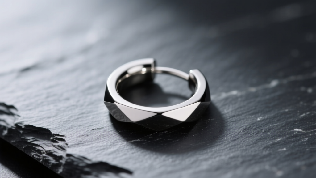 Macro shot of a 16-gauge ASTM F136 titanium seamless hoop earring resting on dark slate with soft directional lighting.
