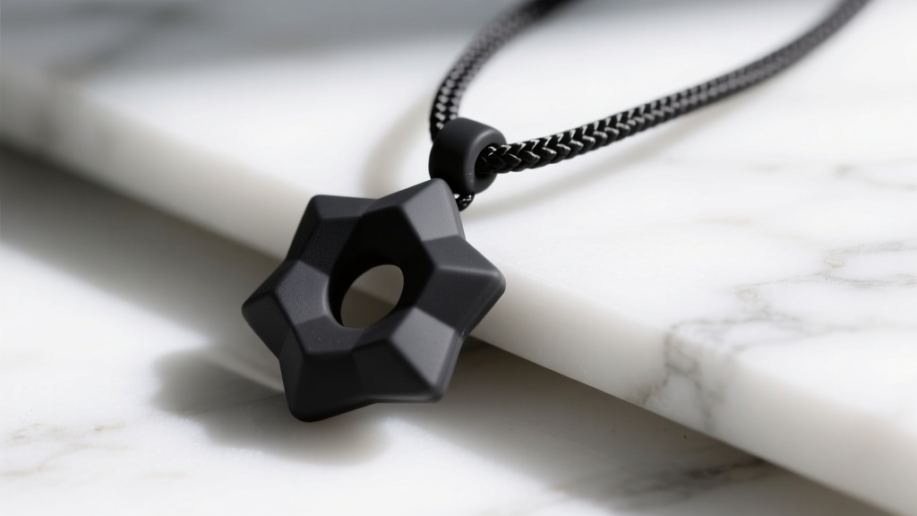 Close-up of a matte black geometric medical-grade silicone chew pendant on a braided nylon cord resting on white marble.