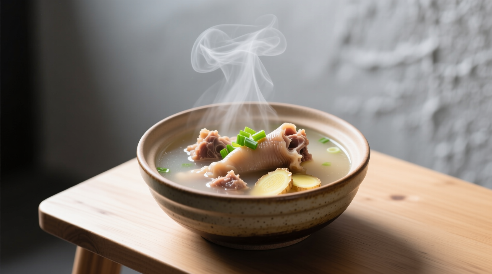 Winter morning bowl of cow foot soup garnished with fresh ginger slices and scallions, showing the rich amber broth and tender meat