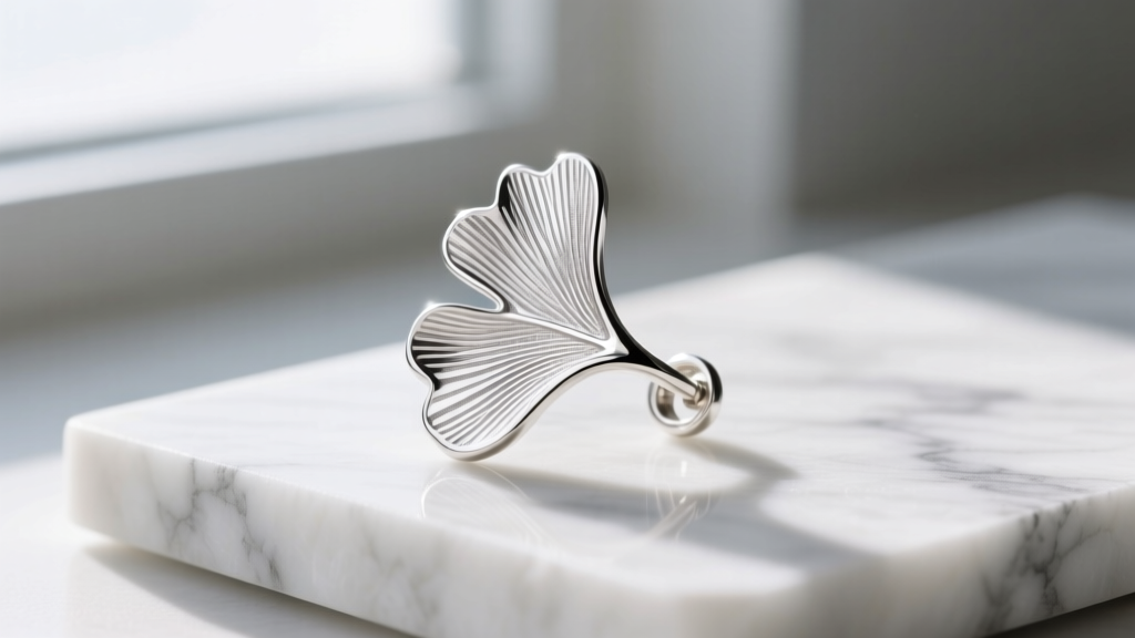 Macro photography of an Argentium silver ginkgo leaf ear cuff, highlighting the bright untarnished metal grain on a marble slab