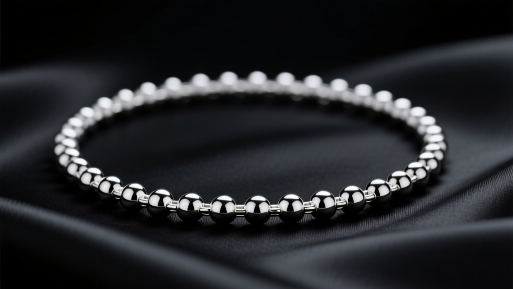 Close-up of a 4.5mm solid sterling silver ball chain necklace resting on black silk fabric with soft, moody studio lighting.