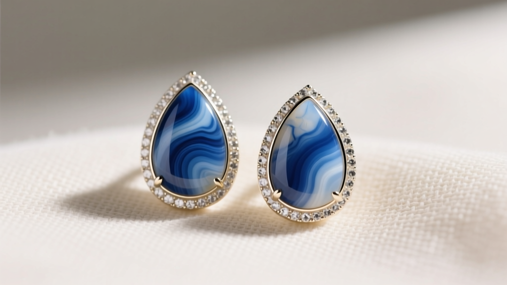 Close-up of a pair of 14k white gold bezel-set blue lace agate teardrop earrings resting on textured cream linen fabric background.