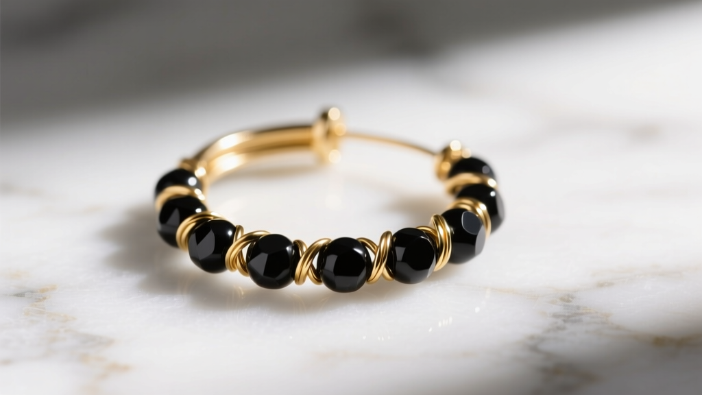 Macro shot of 14k gold-filled wire threaded with matte black onyx beads forming a small continuous hoop earring on white marble.