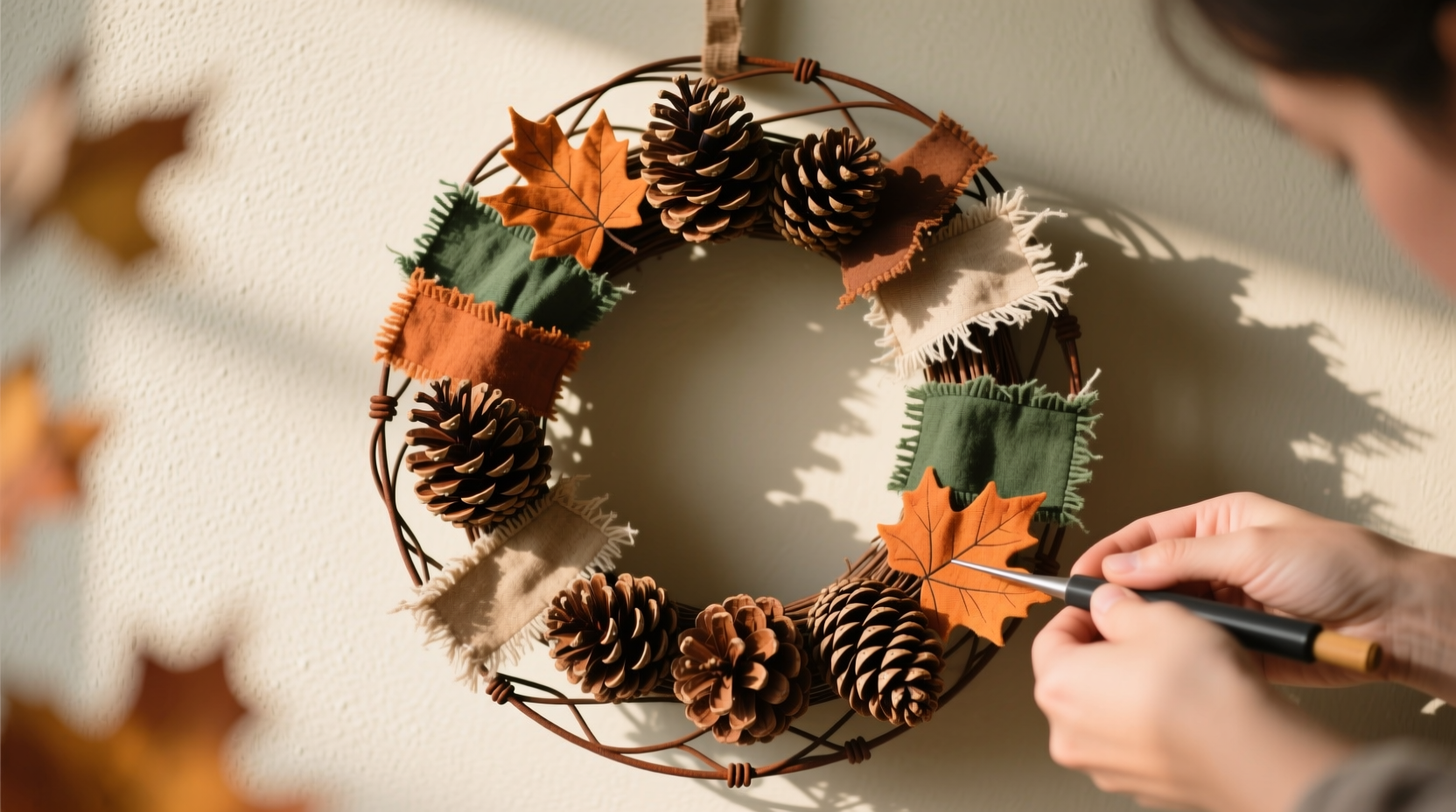 Step-by-step photos showing hands assembling a fall wreath with pinecones and fabric scraps on a wire frame