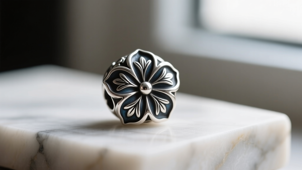 Macro close-up of a hand-stamped sterling silver blossom bead, showing deep oxidized patina and precise silversmith chisel marks