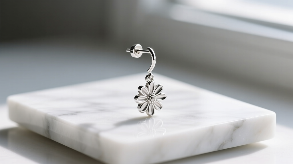 Side profile of sterling silver daisy drop earring showing 20-gauge post and friction back on a white marble jewelry display tray.