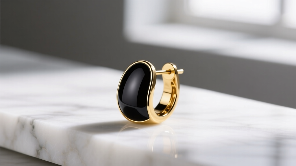 Close-up macro shot of a gold-plated brass designer earring with glossy black cold enamel inlay, resting on a white marble surface.