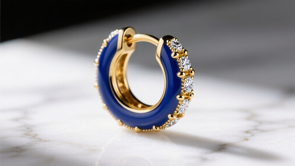 Macro shot of 16-gauge gold huggie earring with deep blue vitreous enamel and white diamond pavé accents on white marble