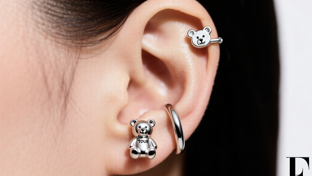 Curated ear stack with a mini TOUS bear huggie on the lobe and a small bear cartilage stud, shot in bright, diffused studio light.