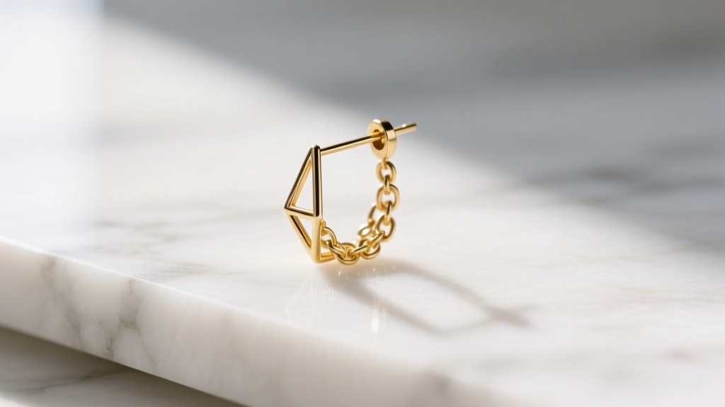 Macro shot of a delicate 14k gold Leru threader earring on white marble, soft morning light highlighting the fine chain links.