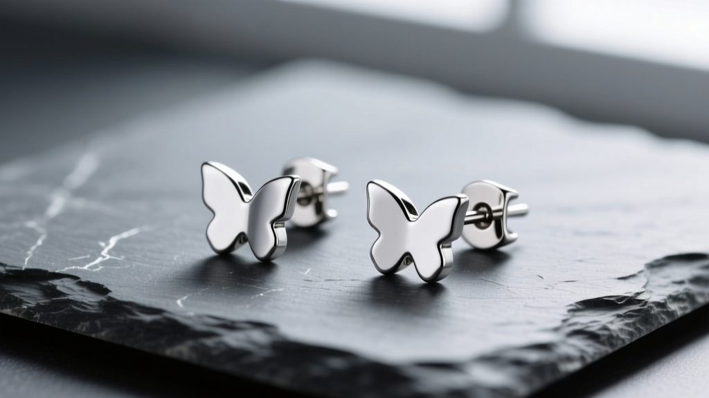 Polished 316L surgical steel stud earrings on slate, showing mirror finish and butterfly backs under soft studio lighting.