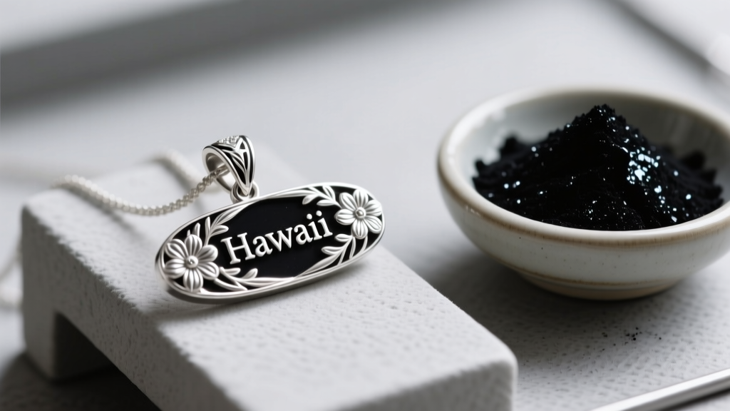 Sterling silver Hawaiian name pendant with floral motifs on a jeweler bench next to a small bowl of black vitreous enamel powder