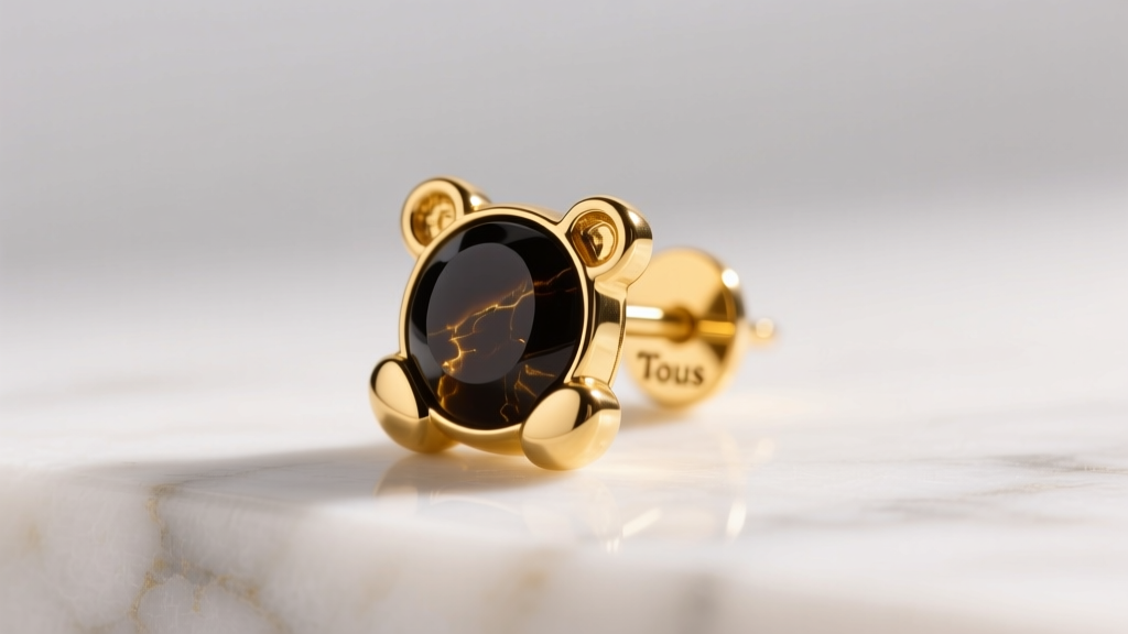 Macro shot of an 18k yellow gold Tous bear stud earring on white marble, warm lighting highlighting the dark onyx inlay