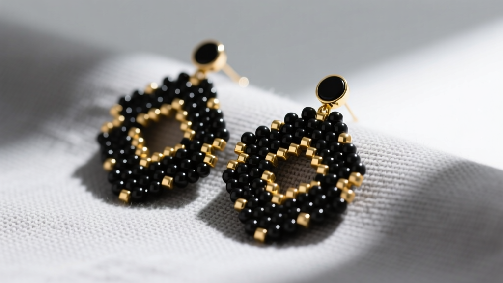 Close-up of geometric brick stitch earrings made with matte black and gold Miyuki Delica beads resting on soft gray linen.
