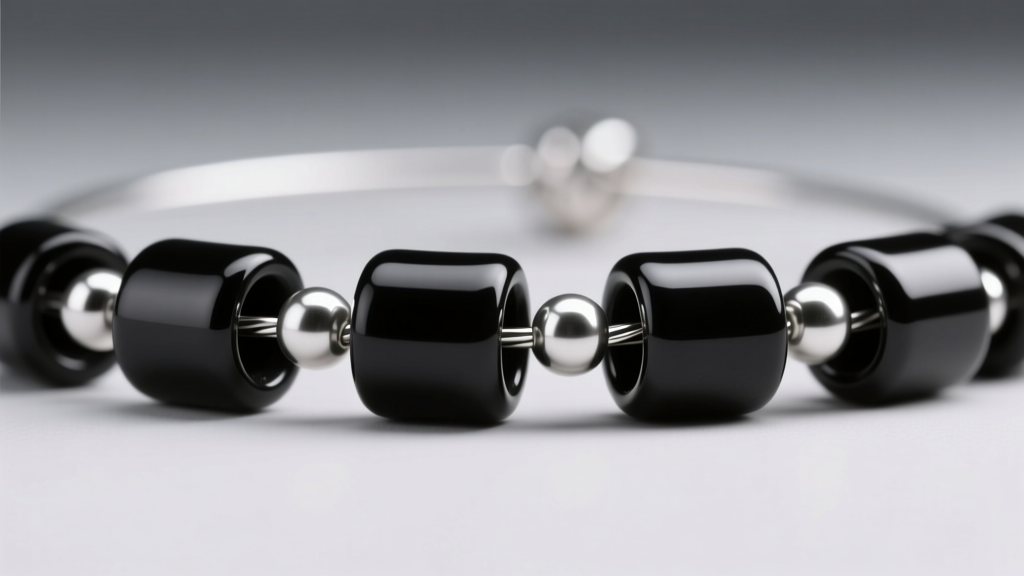 Macro shot of matte black ceramic tube beads interspersed with tiny silver seed beads on a steel stringing wire under studio lighting.