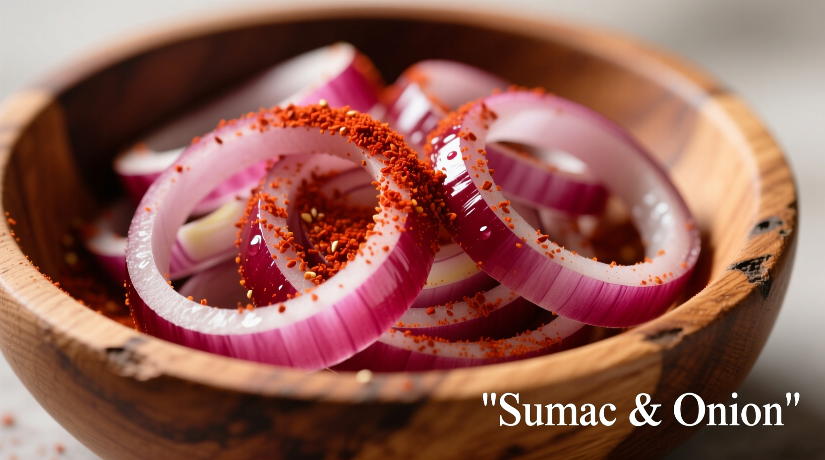 Sumac spice sprinkled over sliced red onions in a wooden bowl