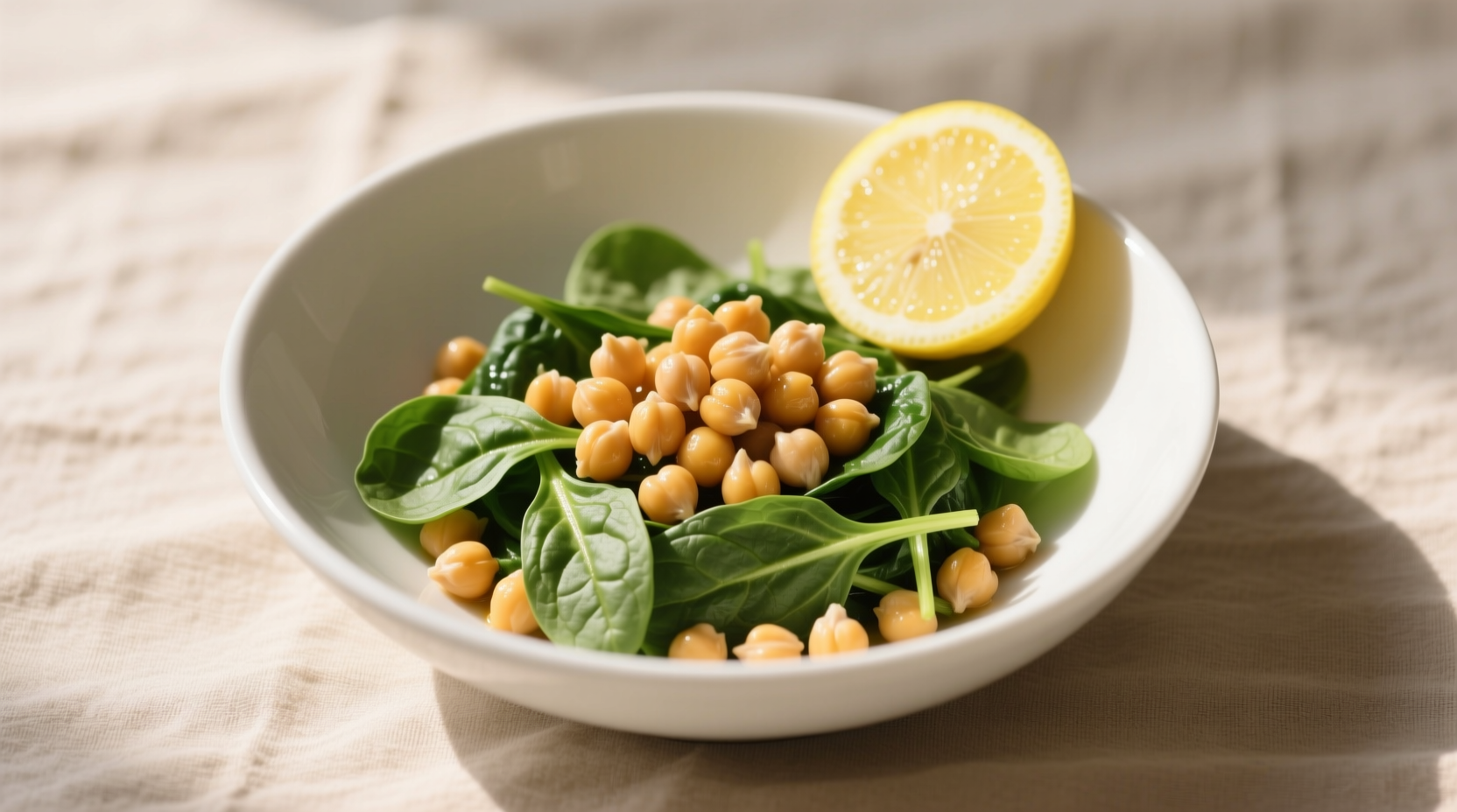 Chickpea spinach dish in white bowl with lemon garnish